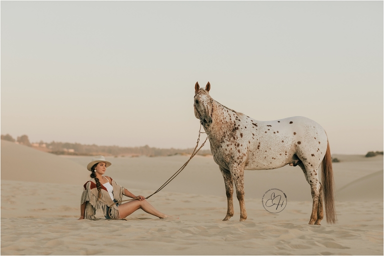woman sitting with Appaloosa horse at a high fashion equine shoot at the Pismo Beach Dunes by Elizabeth Hay Photography