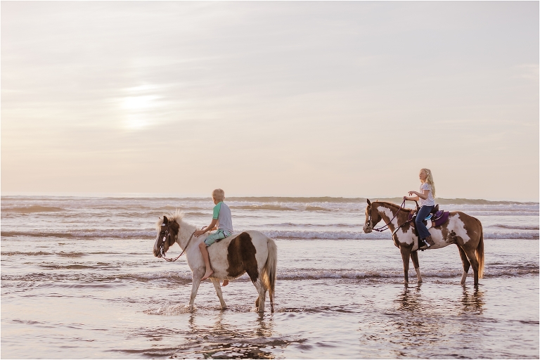 Boy and Girl riding paint horses in the ocean by Elizabeth Hay Photography