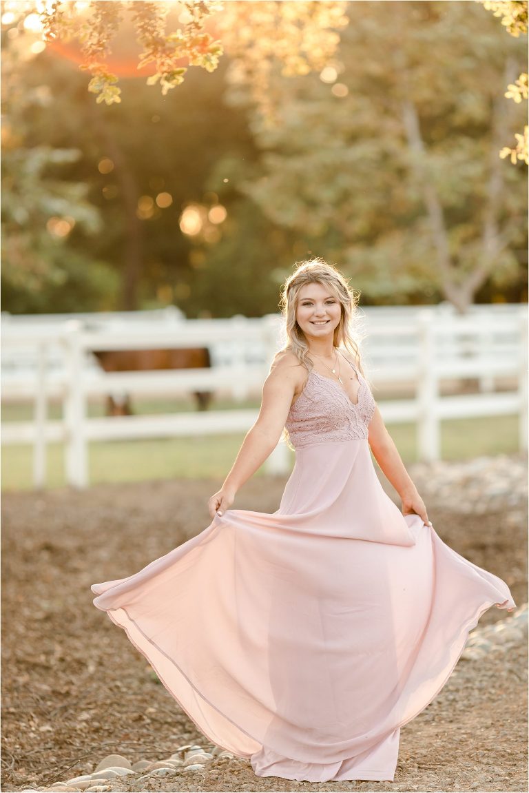 blonde girl in pink dress twirling with horses behind her in a pasture