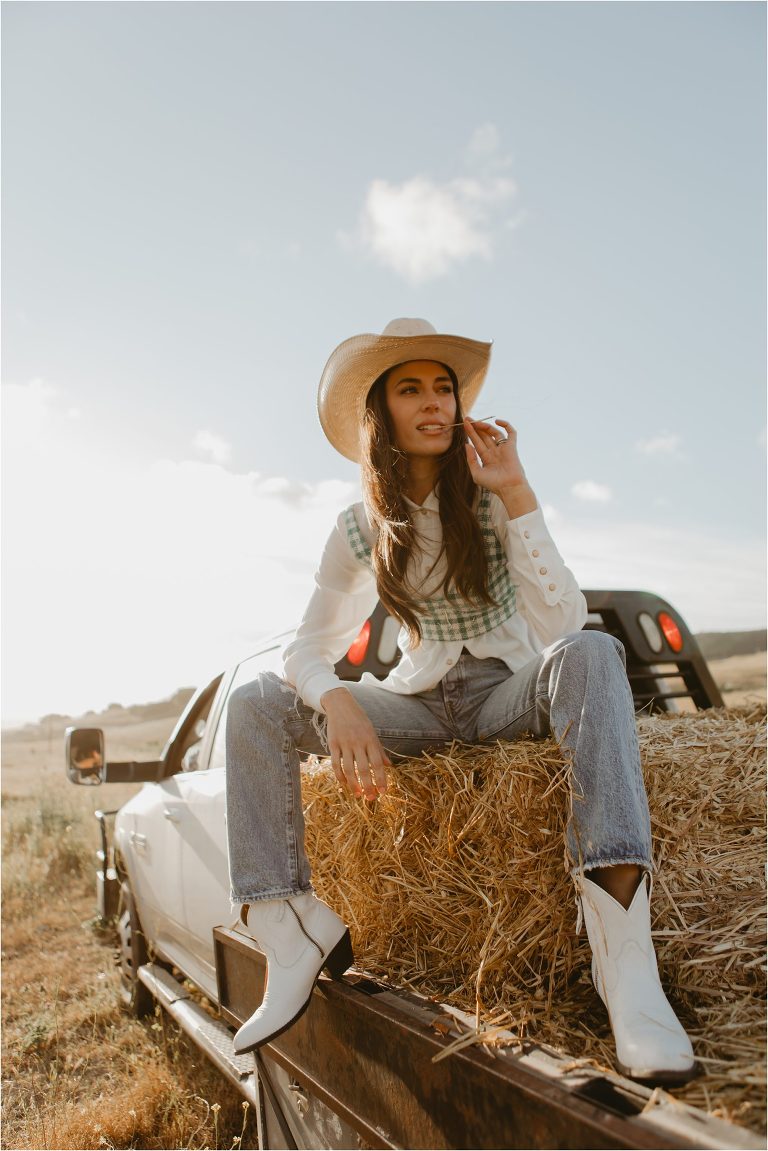 Lindsay Branquinho sitting on a hay bale on the back of a feed truck driving by her husband Luke Branquinho