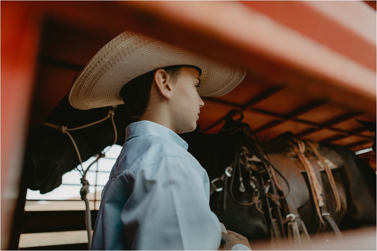 young cowboy helps load horses into red horse trailer