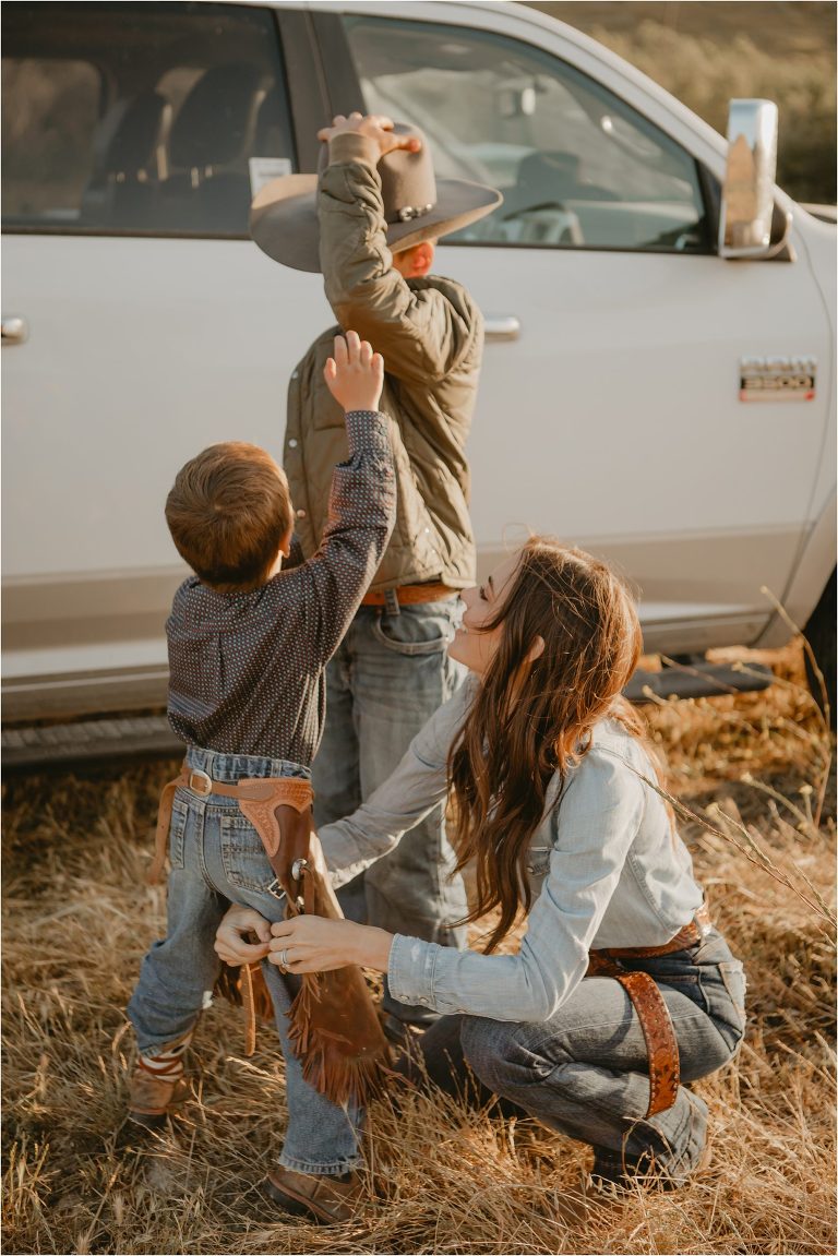 mom helps her two young cowboy get dressed for a ranch family photo shoot