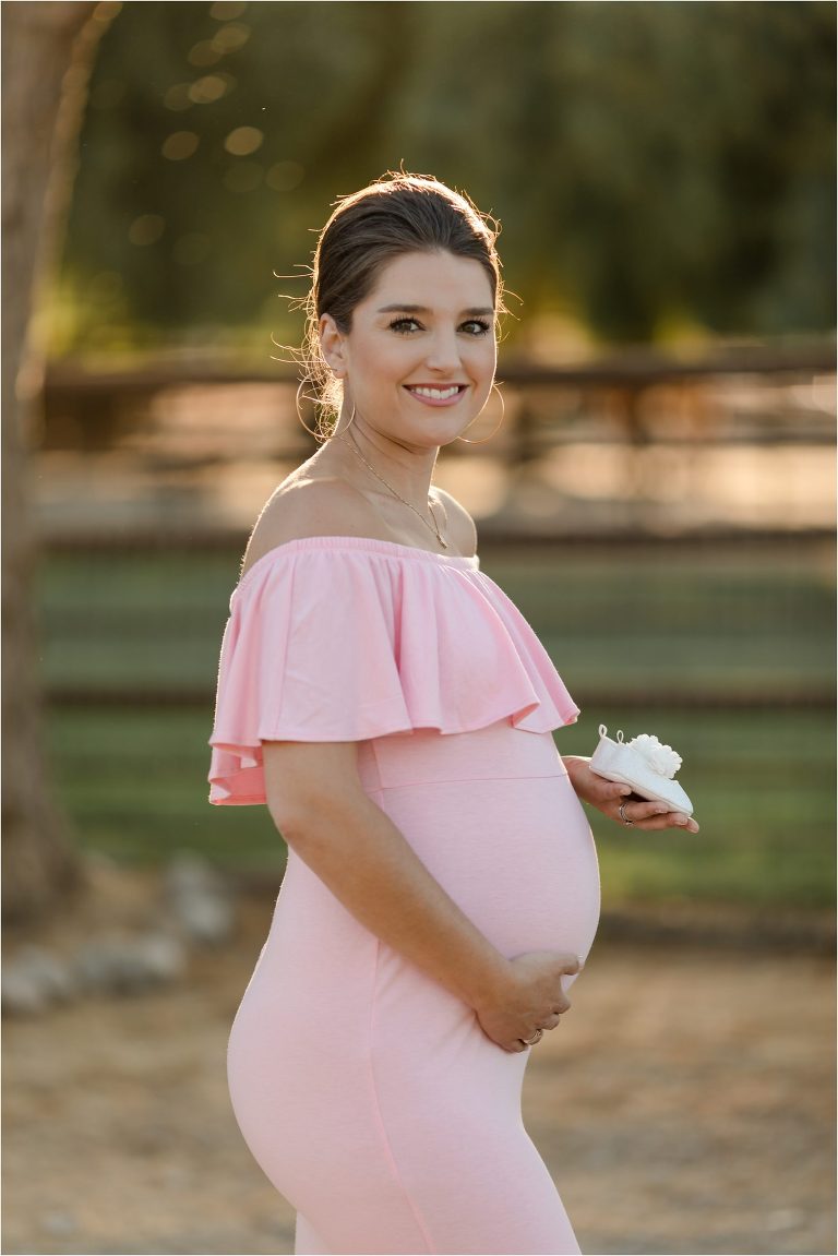Pregnant woman in pink dress holding baby shoes by Elizabeth Hay Photography