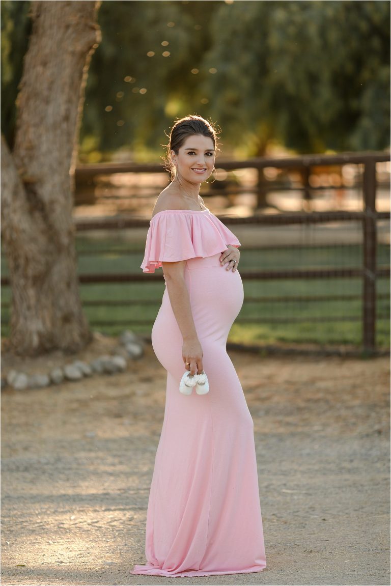 Pregnant woman in pink dress holding baby shoes by Elizabeth Hay Photography