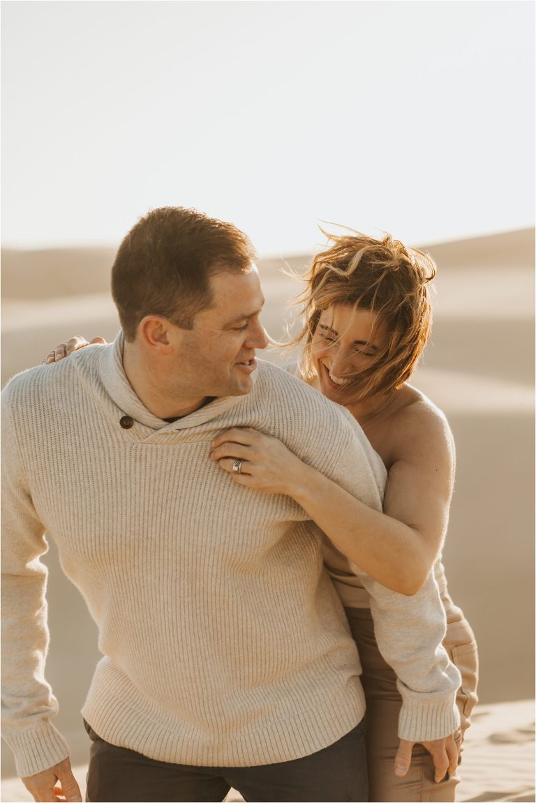 couple hugging and laughing on beach dunes in Pismo Beach California by Elizabeth Hay Photography