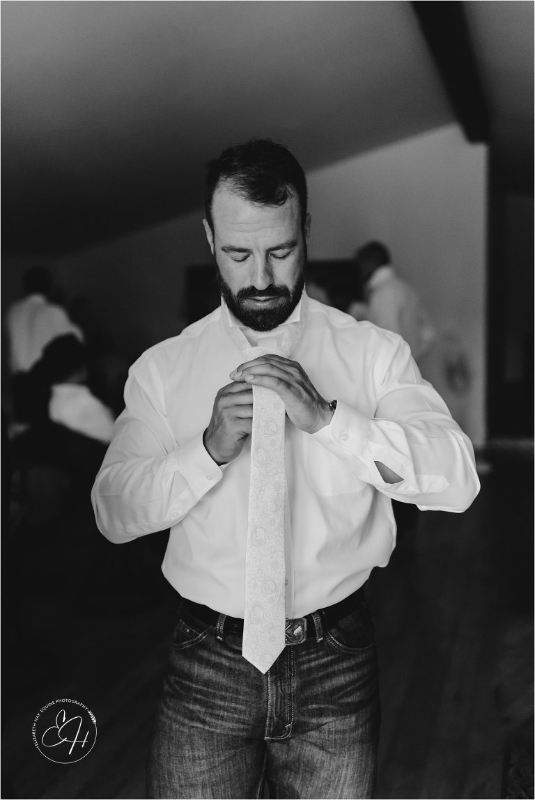 groom tying his tie prior to wedding