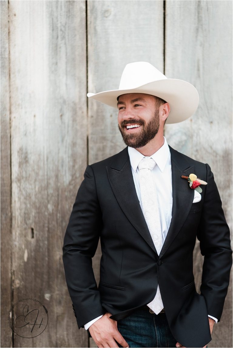 western groom smiling against barn wood wall prior to Morro bay Ranch wedding