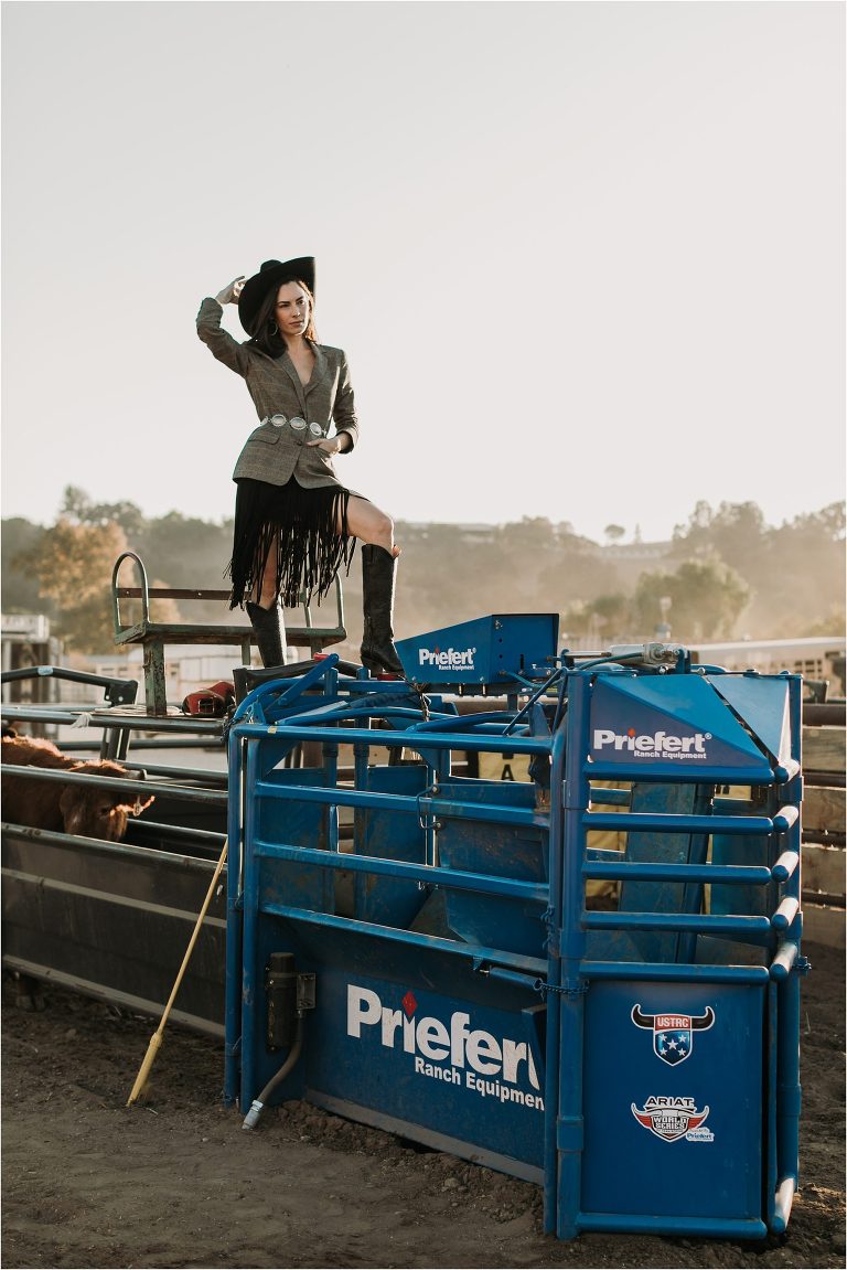 Lindsay Branquinho standing on top of a Priefert Ranch Equipment roping chute wearing a Stetson hat, fringe skirt and tweed blazer by California Equine Photographer Elizabeth Hay Photography. 