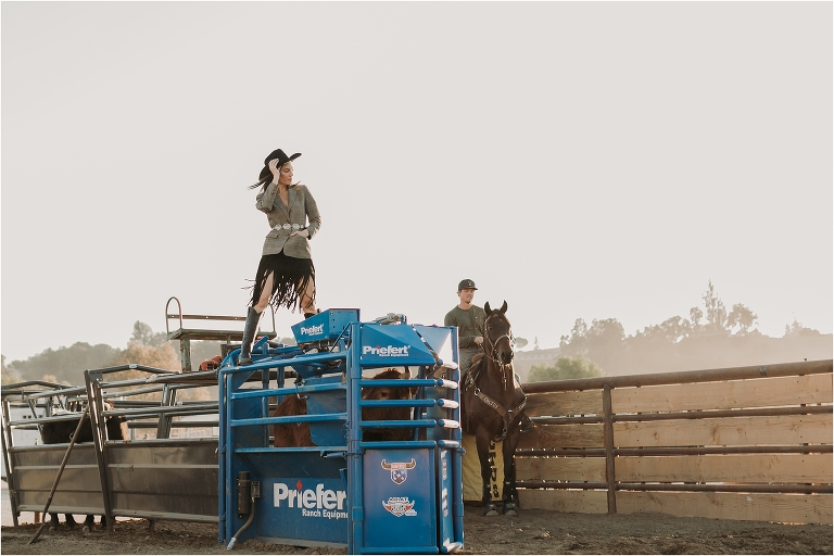 Lindsay Branquinho standing on top of a Priefert Ranch Equipment roping chute wearing a Stetson hat, fringe skirt and tweed blazer and silver belt by California Equine Photographer Elizabeth Hay Photography. 
