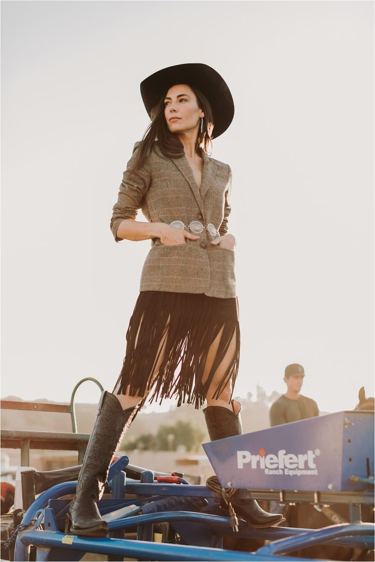 Lindsay Branquinho standing on top of a Priefert Ranch Equipment roping chute wearing a black Stetson hat, fringe skirt, tweed blazer and silver concho belt by California Equine Photographer Elizabeth Hay Photography. 