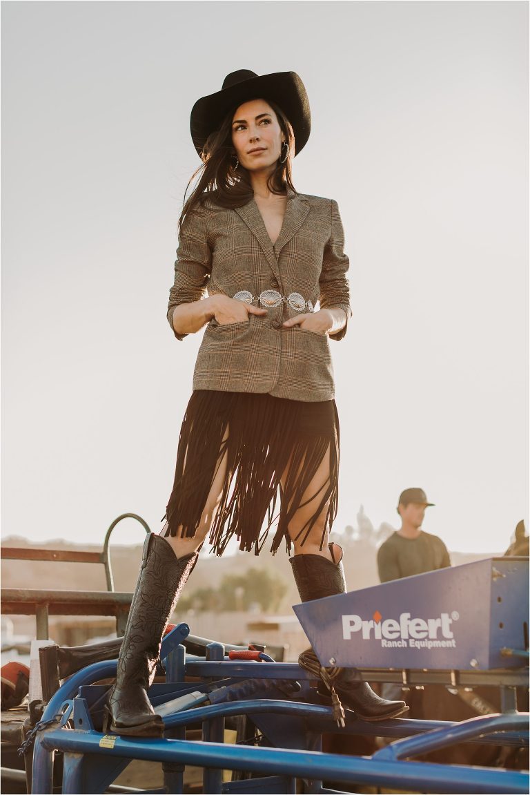 Lindsay Branquinho standing on top of a Priefert Ranch Equipment roping chute wearing a Stetson hat, fringe skirt, tweed blazer and black western boots by California Equine Photographer Elizabeth Hay Photography. 