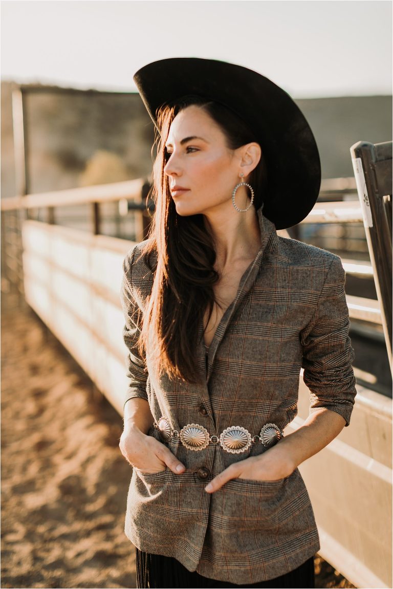 Lindsay Branquinho leaning against a roping chute wearing a Stetson hat, fringe skirt and tweed blazer by California Equine Photographer Elizabeth Hay Photography. 