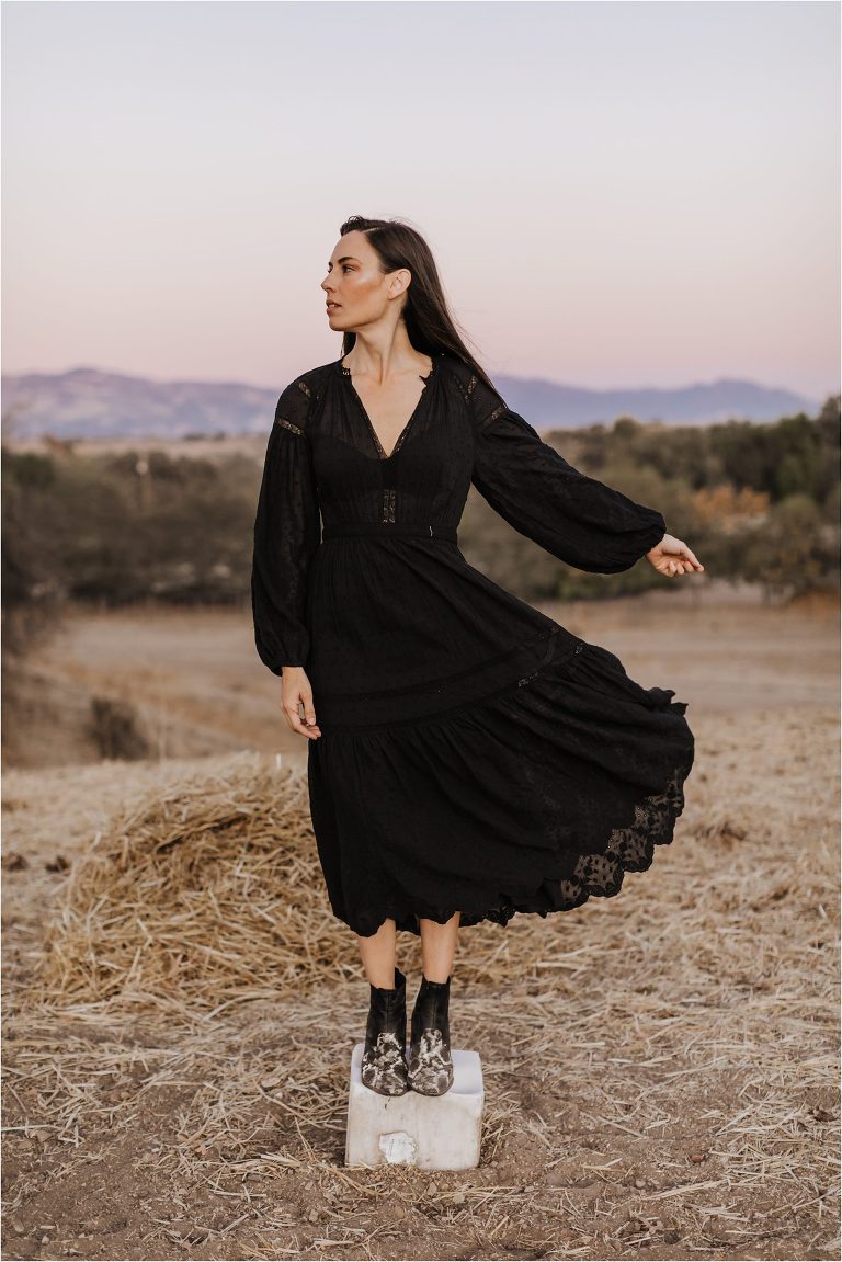 Woman wearing black dress standing in a cow pasture on top of a salt block by Elizabeth Hay Photography. 