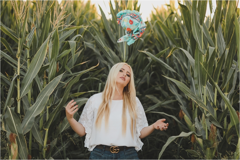 Blonde girl wearing white top and tossing a teal tribal print wild rag in a corn field by California Equine Photographer Elizabeth Hay Photography.