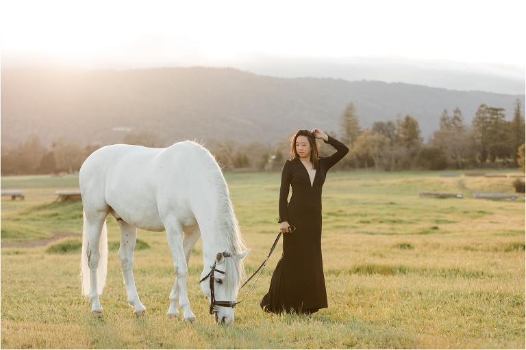 Woman wearing a black deep v-neck dress and white horse in an open eventing field by California Horse Photographer Elizabeth Hay Photography.